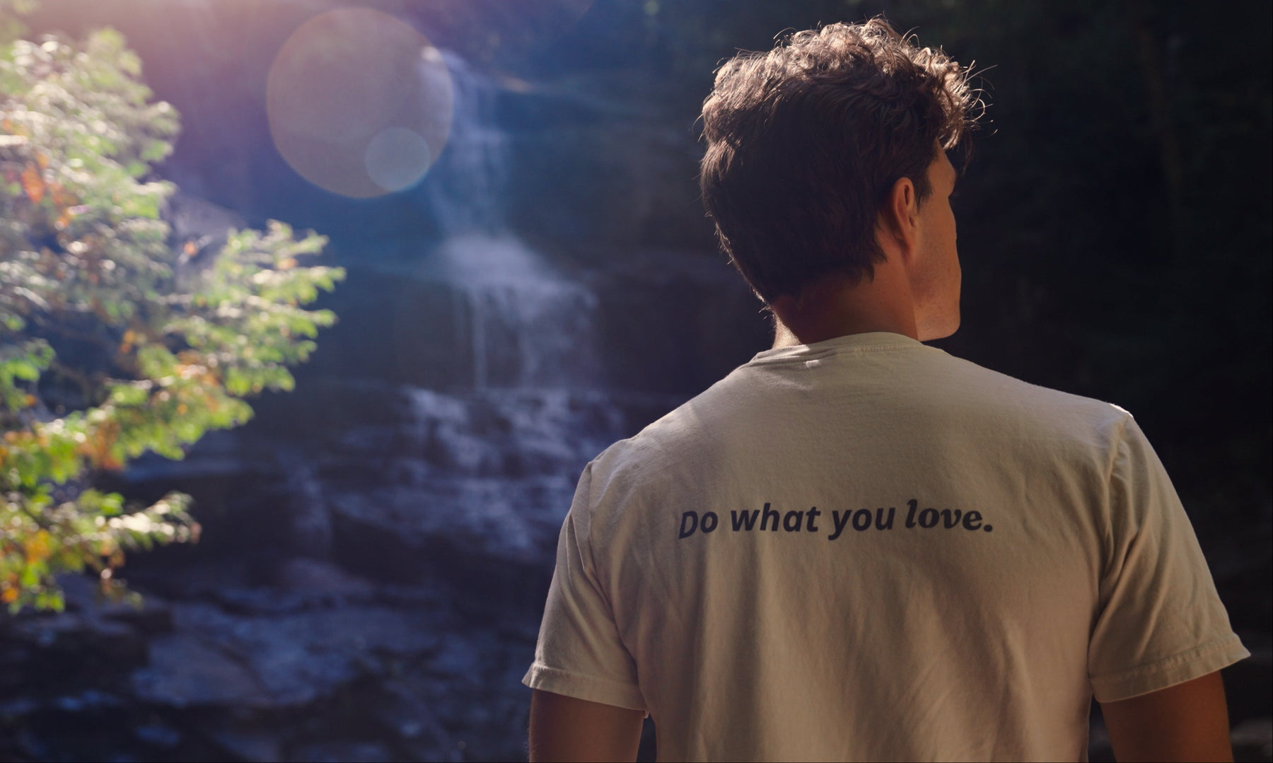 Person wearing a shirt with 'Do what you love.' text, standing in front of a waterfall.